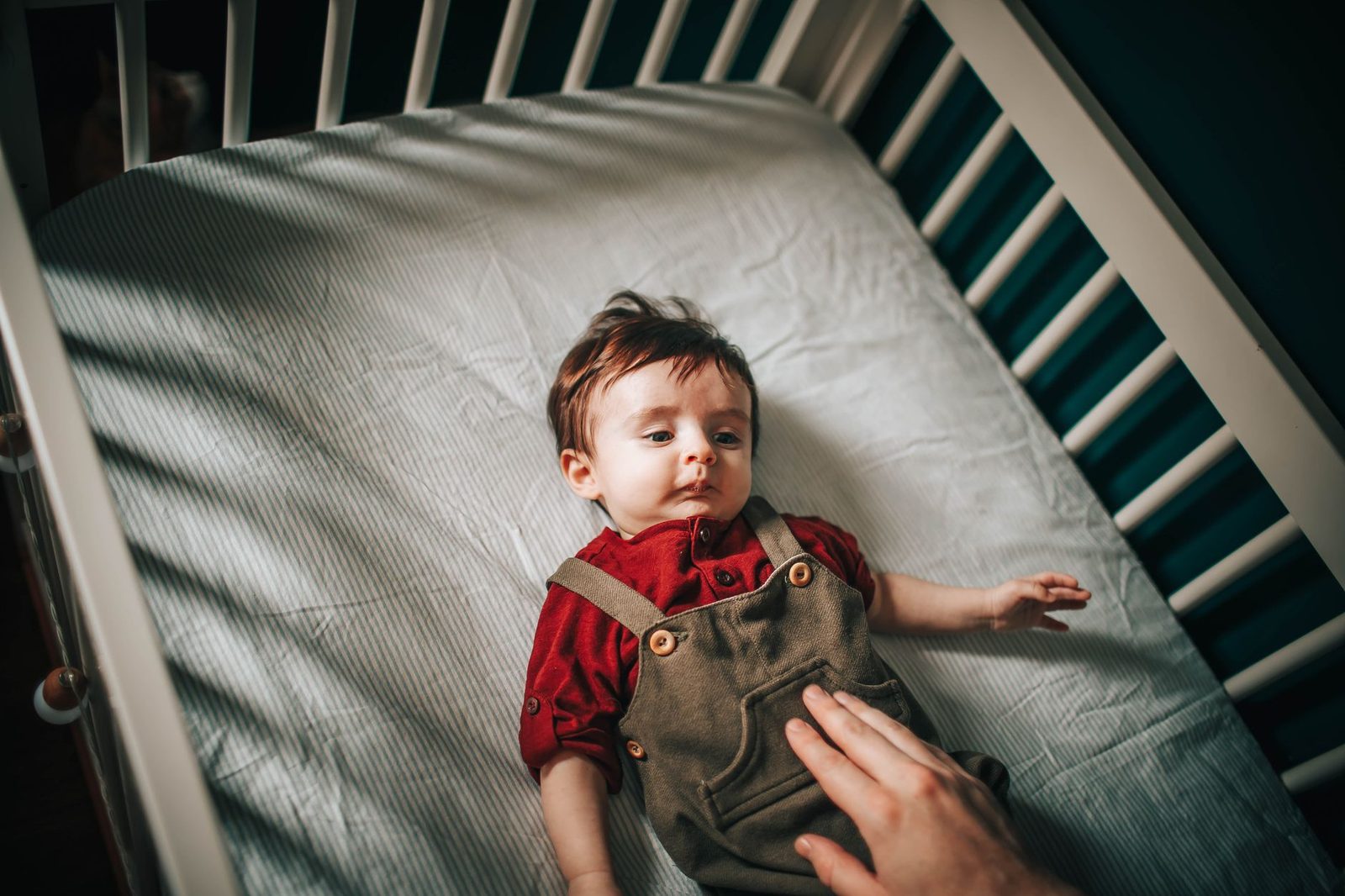 Wacht eerst even af en troost rustig als je baby echt wakker is Baby ligt op de rug in een leeg bedje terwijl een ouderhand hem rustig troost