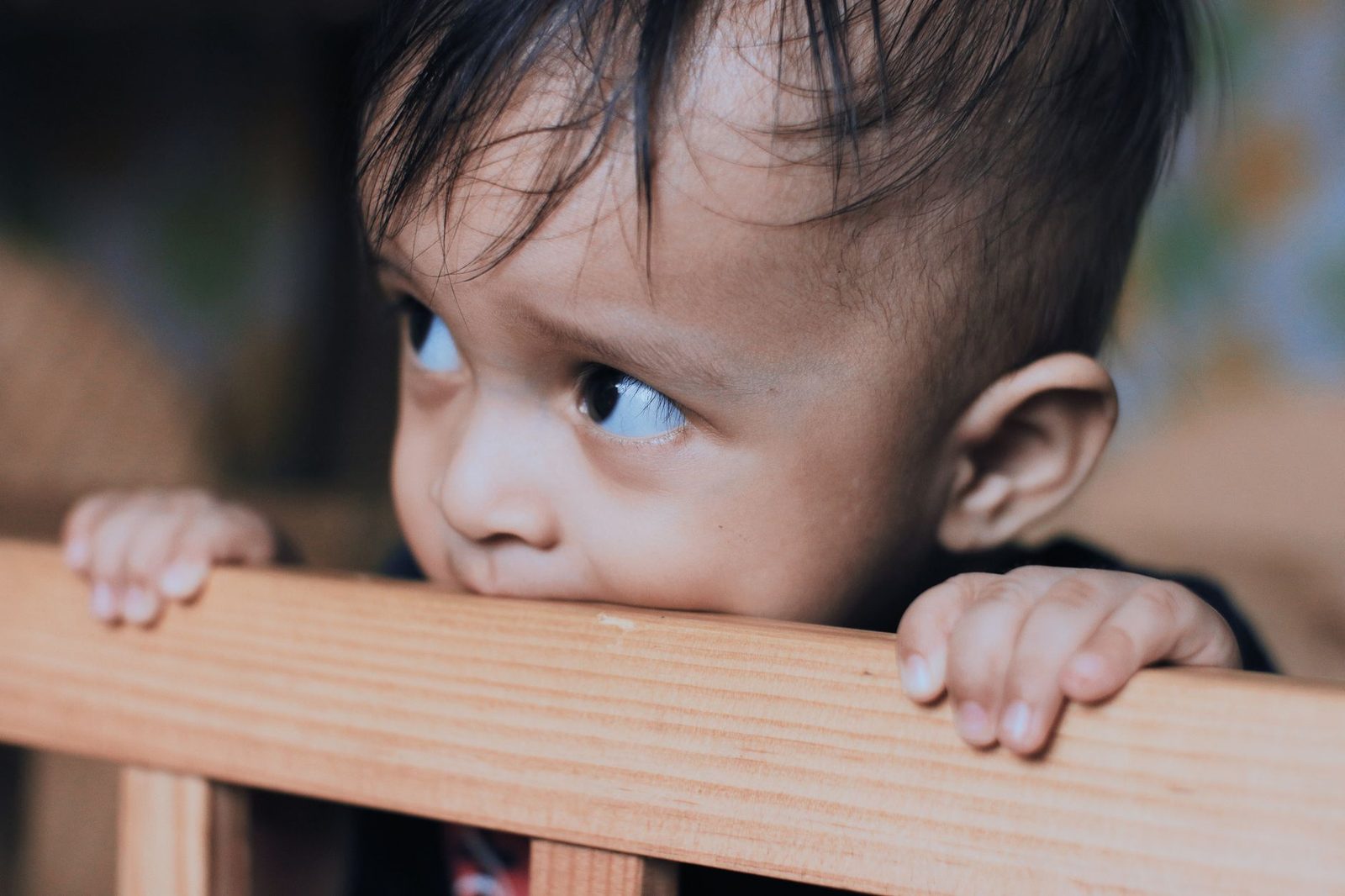 Op alles bijten hoort bij de symptomen van doorkomende tandjes Baby bijt op de houten rand van de box, een klassiek symptoom van doorkomende tandjes